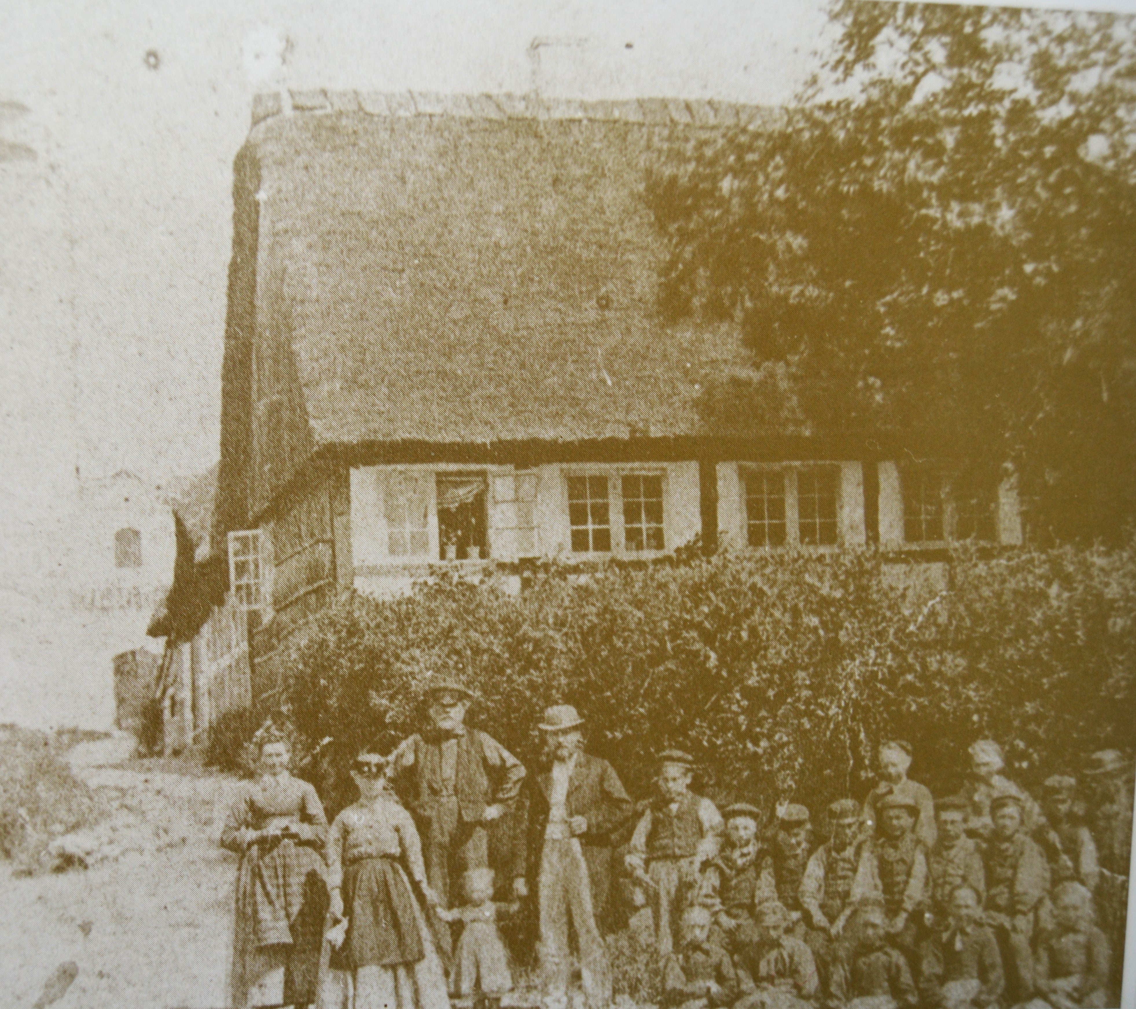 1870-74 Thunø Skole. Forrest tv. står tj.pigen Stine Hansen, fru Kock og lærer Kock m. deres barn. Lige bag postbesørger Ole Kjeldsen. Elever bagerst: Frederik Johansen, Stine Jensen og Andrea Madsen. Midt.rk.: Marius Jørgensen, Morten Hansen, C.M. Kjeldsen (Unge Kjeldsen), Christian Jensen, Kresten Jørgensen, Peter Petersen. Forr.rk.: Frederikke Bielenberg, Rasmine Christensen, Juliane Petersen, Ane Olesen og Johanne Madsen.